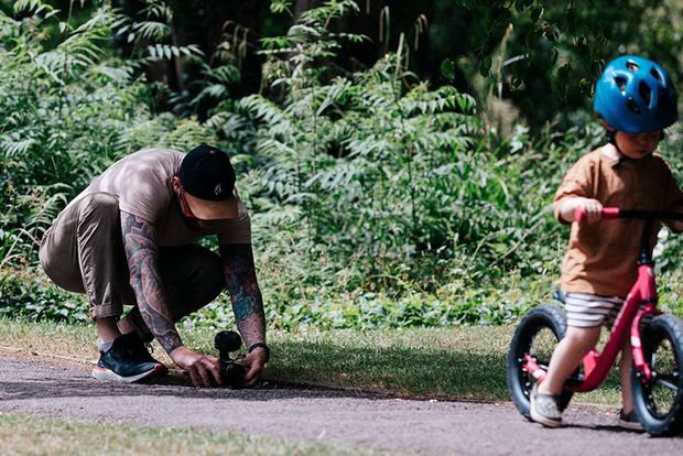 Stef Michalak holding a Canon EOS M50 camera at floor level to film his son's first ride on a balance bike. 
