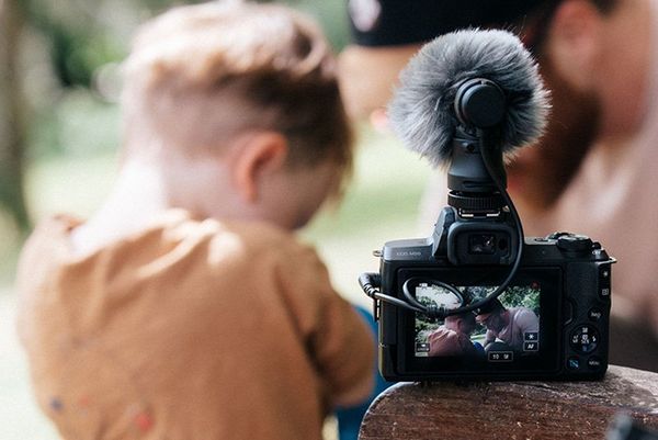 The Canon EOS M50 with the Canon DM-E100 mic attached, positioned on the arm of a bench behind Stef Michalak and his son. 