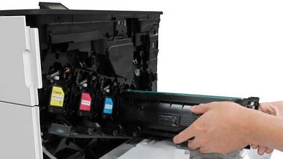 A Canon laser printer with the toner shelf open and the black toner being inserted.