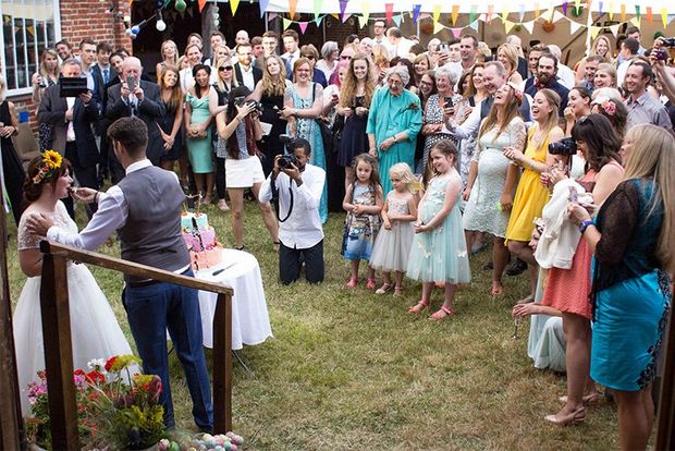Wedding guests gather around the bride and groom as they cut the cake.