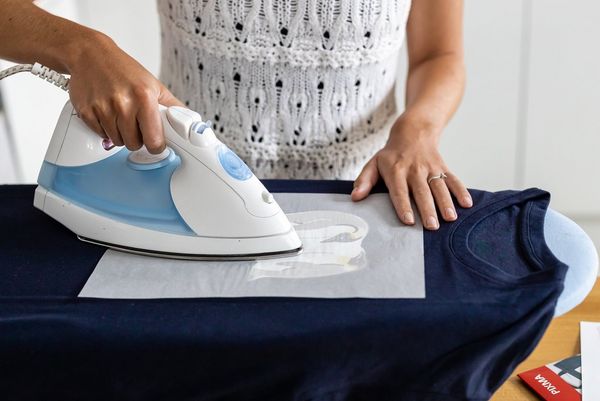 A woman irons an iron-on transfer onto a dark t-shirt.