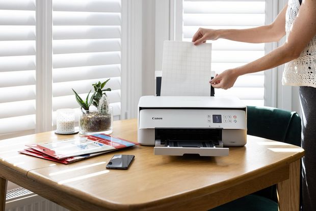 A woman loads a sheet of iron-on transfer paper into a Canon PIXMA TS5350 printer.