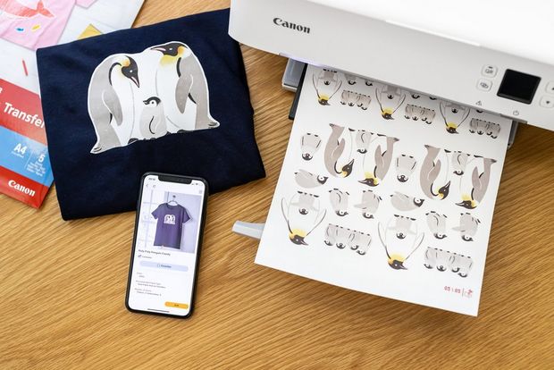 A sheet of iron-on transfers on a printer tray next to a smartphone and a t-shirt.