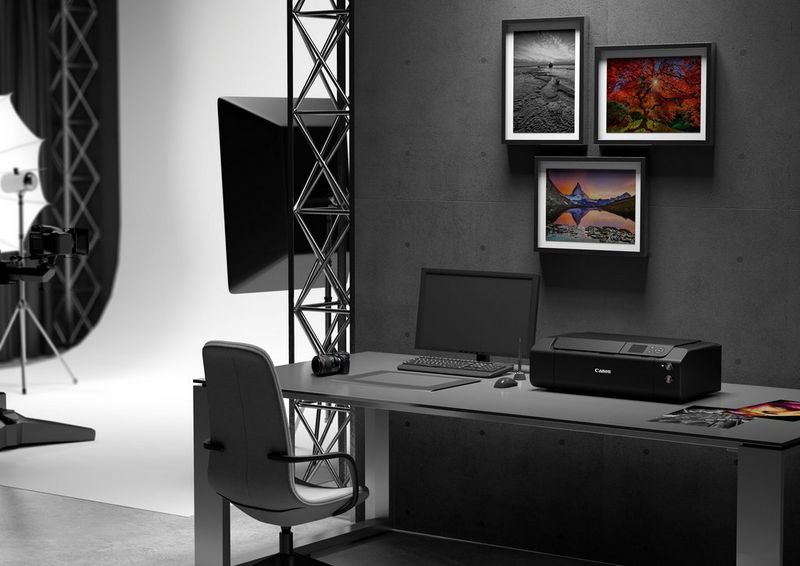 Une imprimante photo Canon imagePROGRAF PRO-300 posée sur un bureau dans un studio de photographie principalement en noir et blanc. À ses côtés, un ordinateur portable et des photos imprimées en couleur.
