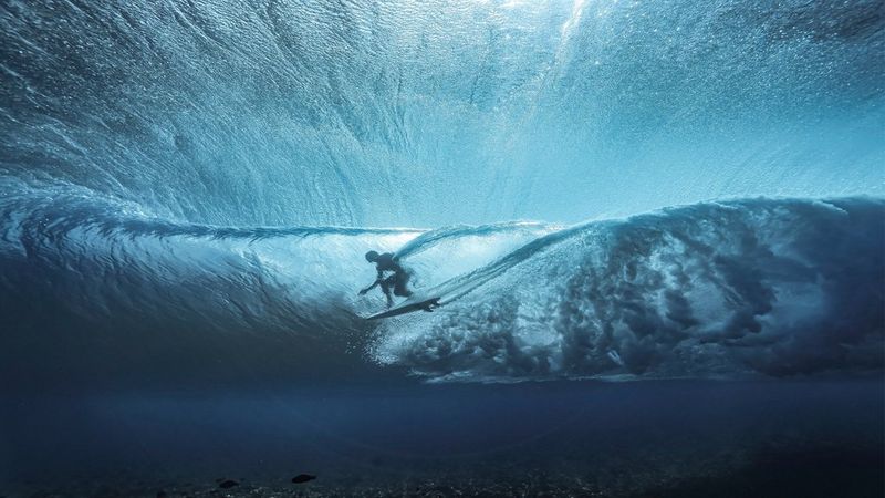 Ein im Schatten gelegener Surfer reitet eine gigantische Welle.