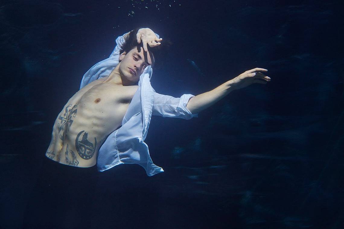 Ukrainian ballet dancer and actor Sergei Polunin throws his arms above his head as he poses underwater for Italian Vanity Fair in suit trousers and an open blue shirt, exposing his tattooed stomach beneath.
