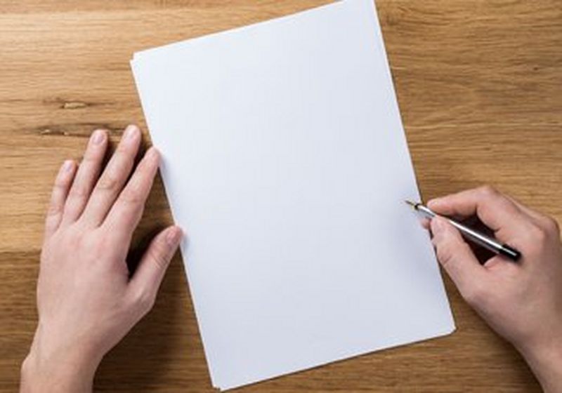 A pair of hands on either side of a sheet of blank white paper. One hand holds a pen