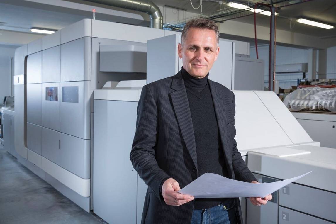 Man stands front of varioprint i300 digital printing press holding large piece of paper