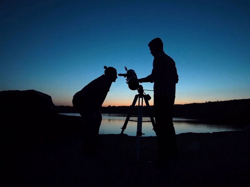 man looking through telescope at sunset