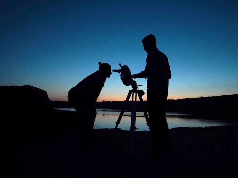 Man looking through telescope at sunset with a friend