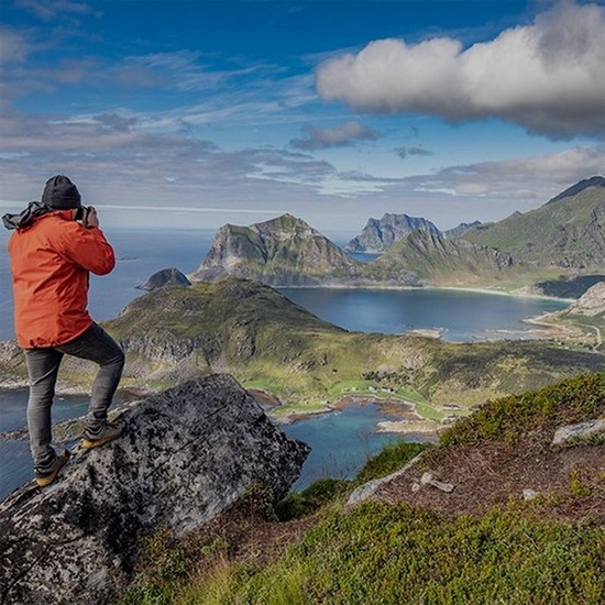man orange jacket shooting coastal mountain landscape