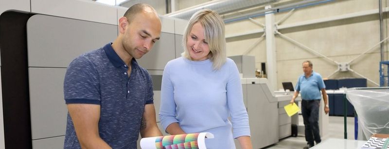 Man and woman look through a book printing catalogue at a large desk