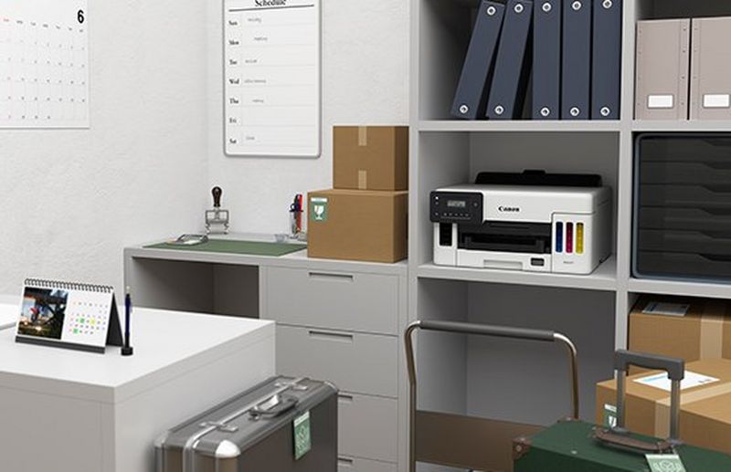 A small office with a printer positioned in the middle compartment of a grey wall unit.