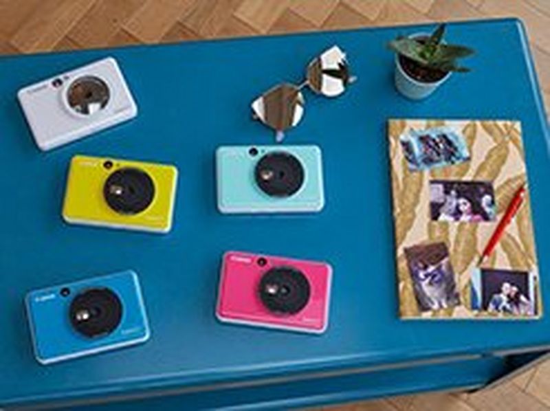 Canon Zoemini C and Canon Zoemini S on a table with a notebook with pictures stuck to it.