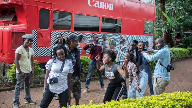 Ten young people having fun in front of a Canon branded double decker London bus.