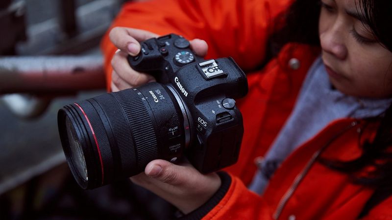 A person holds a Canon EOS R6, looking at the digital display.