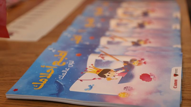 Colourful printed children’s books with Arabic text on the cover lie on a wooden table.