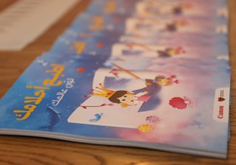 Auf einem Holztisch liegen bunte Kinderbücher mit arabischem Text auf dem Einband.