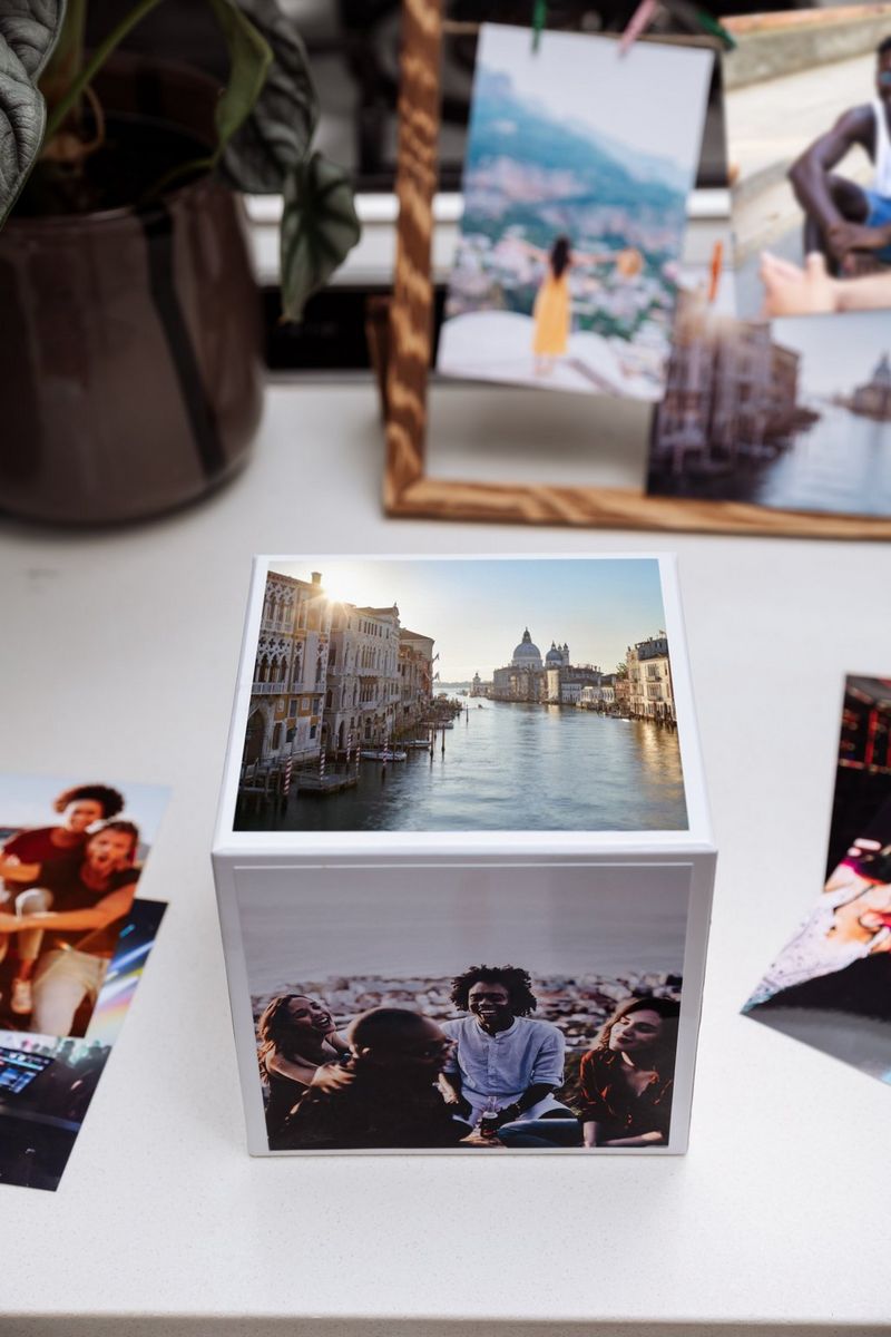 Un Canon Photo Cube sur une table, avec une photo de Venise sur le dessus et un groupe de personnes sur le côté. D'autres impressions sont visibles à l'arrière-plan.