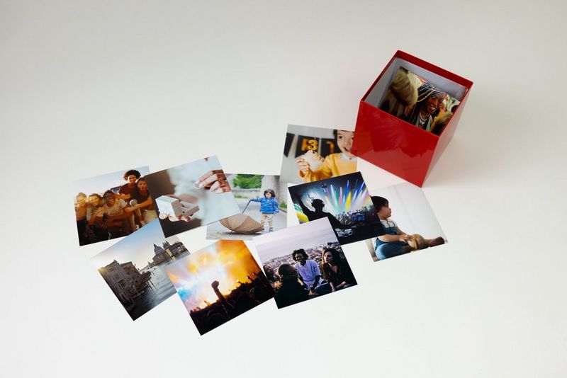 Photographies éparpillées sur la table, en pile, avec un Canon Photo Cube contenant d'autres photographies.