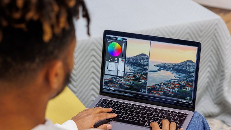 A black man editing and comparing picture of seascape in Picture Style Editor software on the laptop.