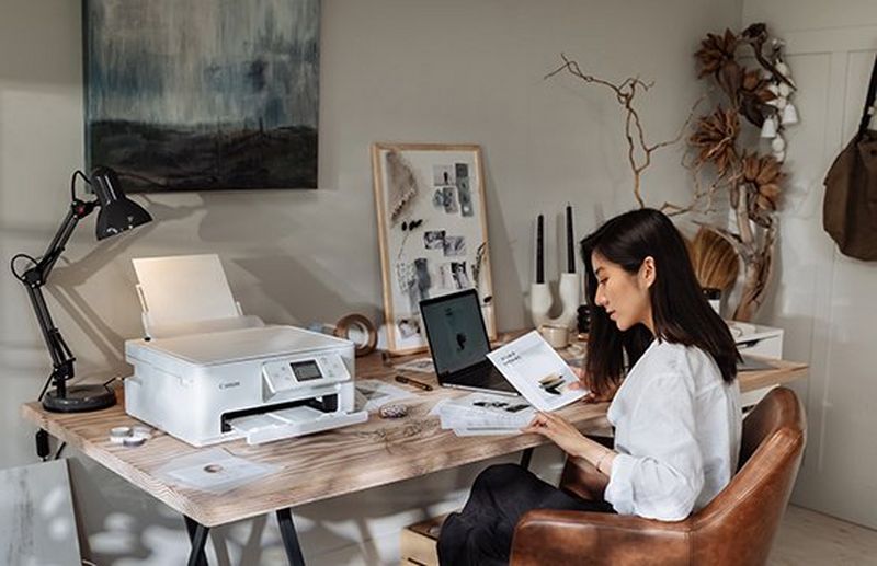 A woman looks at a pile of papers, a Canon PIXMA printer and other stationery sitting on the table.