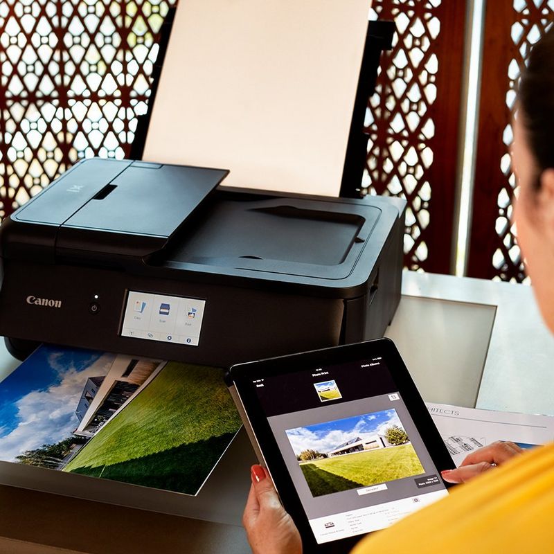 A woman holding a tablet with a picture on it. Printer is visible in the background.