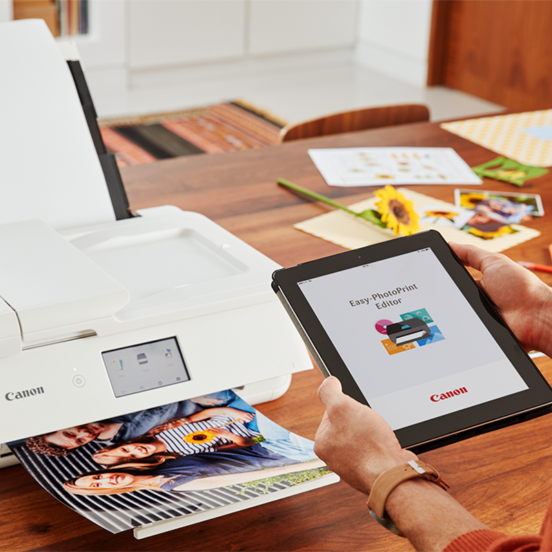 A woman holding a tablet with an icon of the app showing on it. White printer is visible in the background.