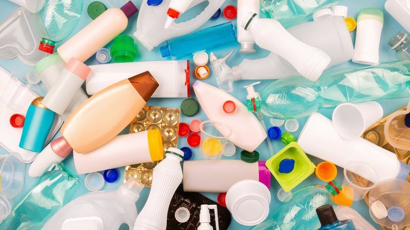 A mess of plastic bottles, cups, containers, lids and caps of assorted colours, all spread out across a table and photographed from above