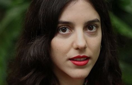 Portrait of a woman with dark hair and a red top, against blurred green plants.
