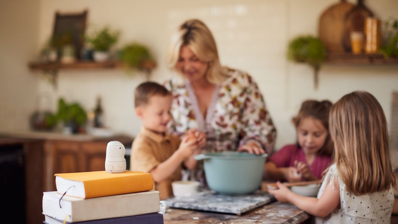 تقف امرأة وأطفالها الثلاثة حول وعاء خلط في المطبخ ويستعدون لتحضير المخبوزات. كاميرا PowerShot PX موضوعة على حزمة كتب تواجهها.