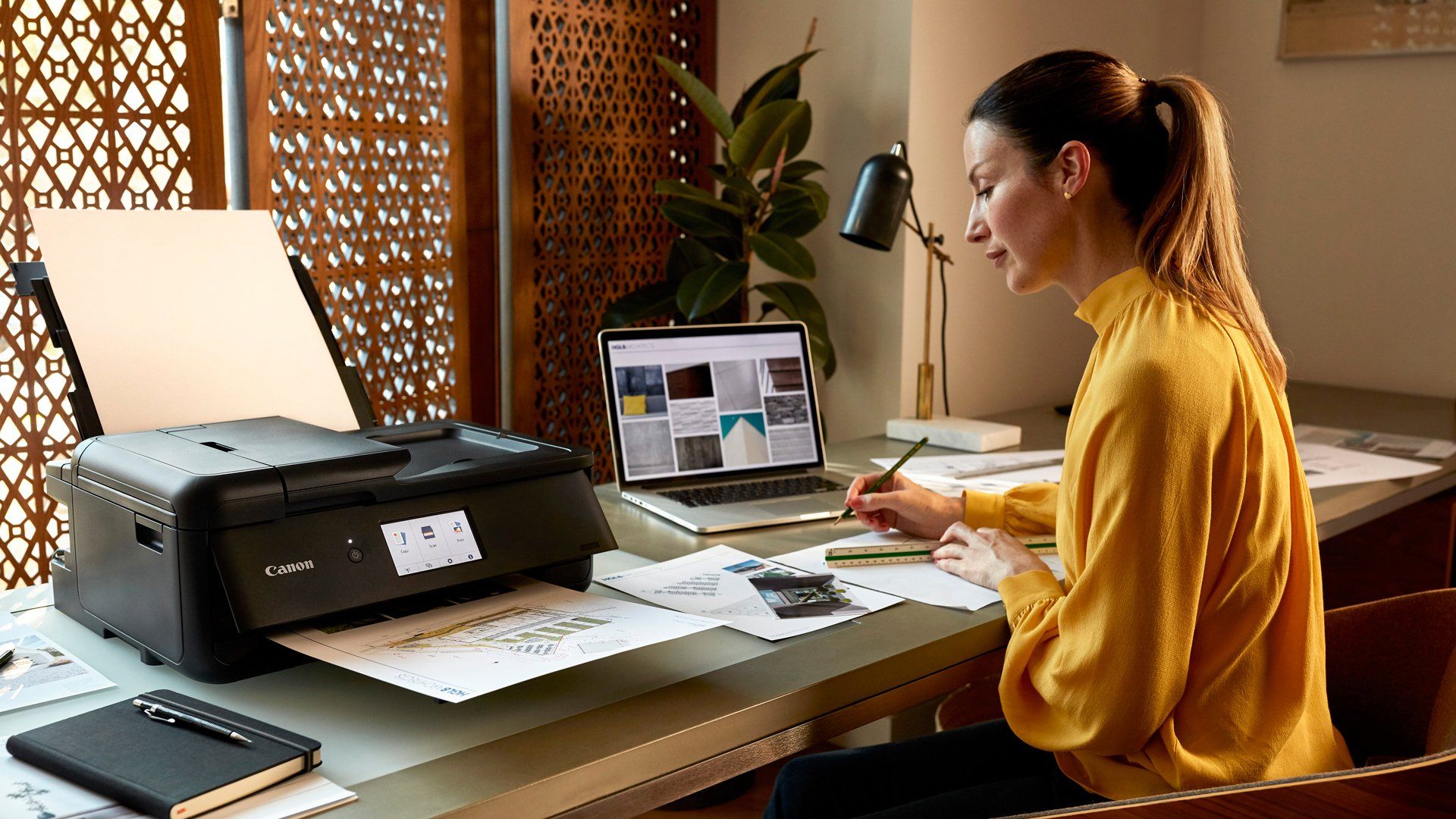A female business owner prints with PIXMA TS9550 while drawing and using a ruler at her desk.