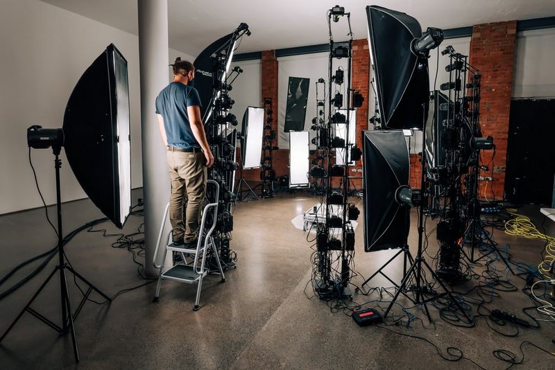 A technician on a step-ladder adjusts one of a large number of lights and camera arrays positioned in a circle around a flat scissor lift.