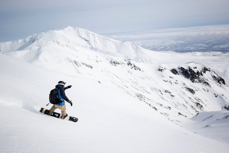 Alex Wykes snowboarding down a mountain carrying a Canon EOS-1D X Mark III.