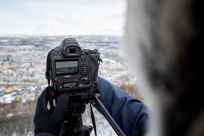 The rear screen of a Canon EOS-1D X Mark III being operated by a person wearing gloves in a snowy landscape.