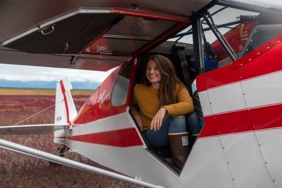 Photographer Acacia Johnson sits in a grounded light aircraft, smiling and looking out of the open door.
