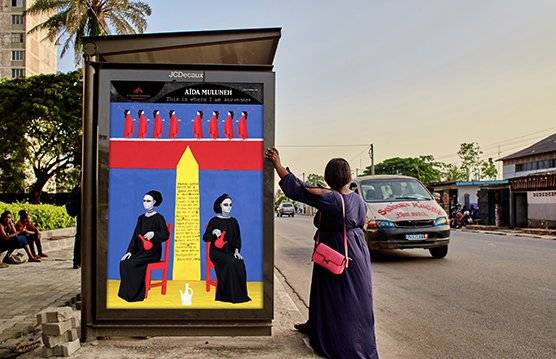 A woman leans up against a bus stop displaying photographer A?da Muluneh's 2022 artwork This Is Where I Am as a car drives by.