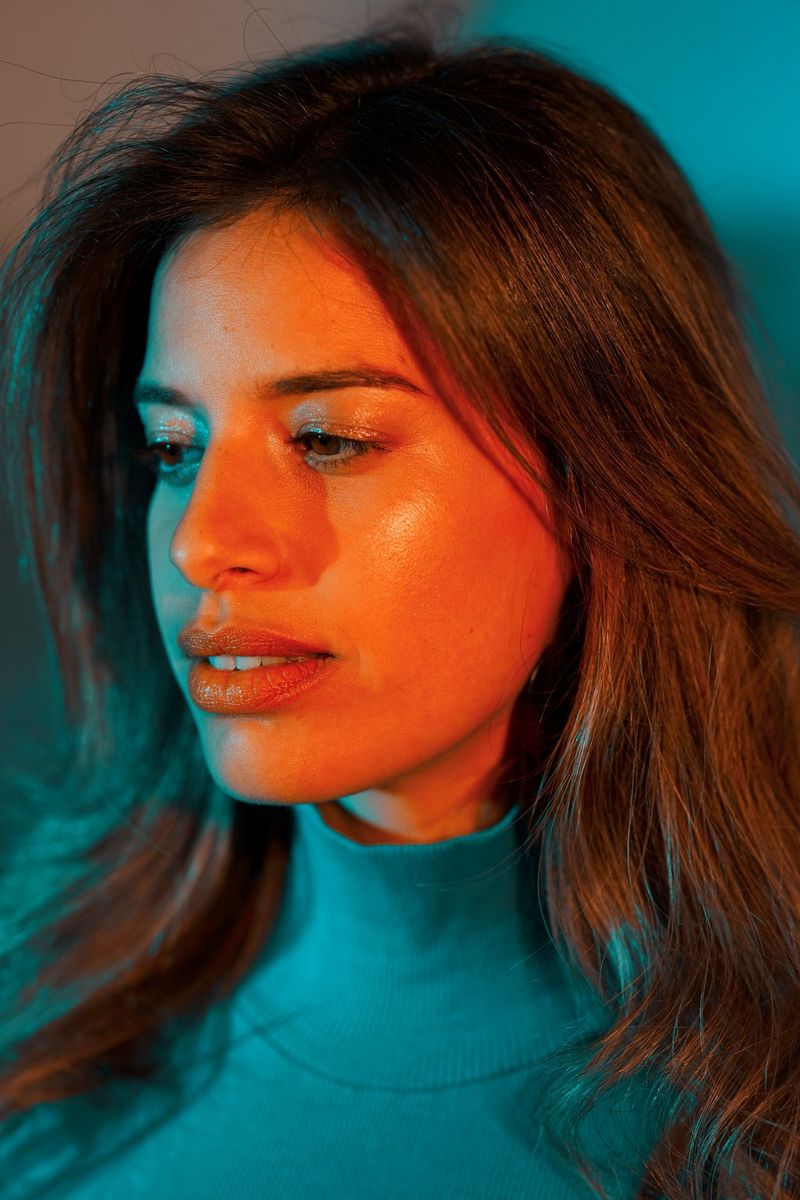 Portrait d'une femme aux cheveux longs vêtue d'un pull à col montant turquoise, la tête légèrement tournée sur le côté.