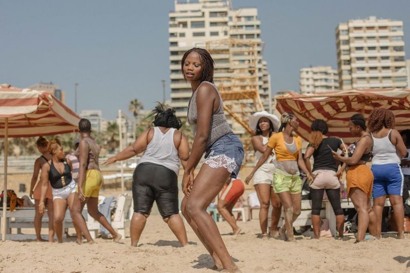 Une femme dansant sur une plage au Liban avec un groupe de personnes sous de grands parapluies rayés derrière elle.