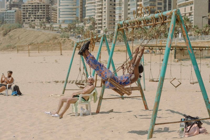 Sur la plage, un homme portant une casquette de baseball regarde une femme sur une balançoire sur une aire de jeux.