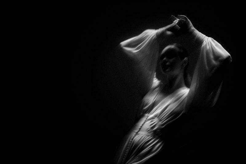 Image en noir et blanc d'une femme lors d'un mariage, qui danse seule les bras en l'air. L'arrière-plan est noir et elle est le seul personnage de la photo.