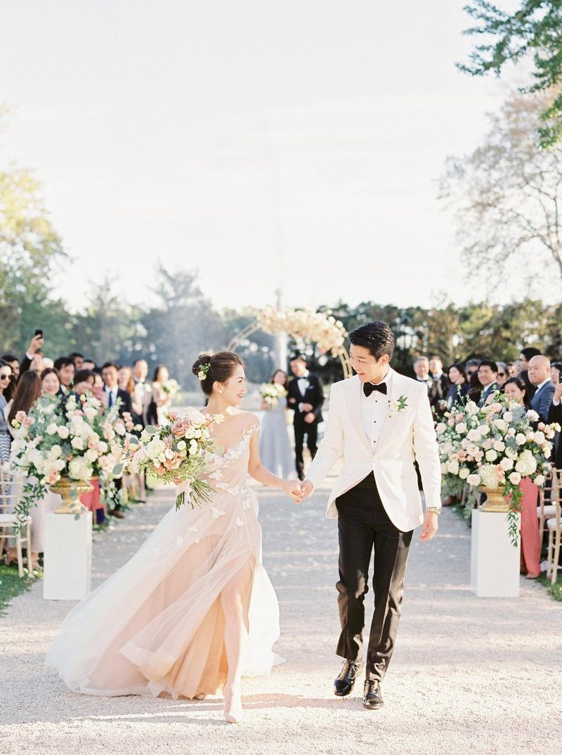 Photographie en couleurs de mariés marchant le long d'une allée devant les membres de la famille qui se réjouissent.