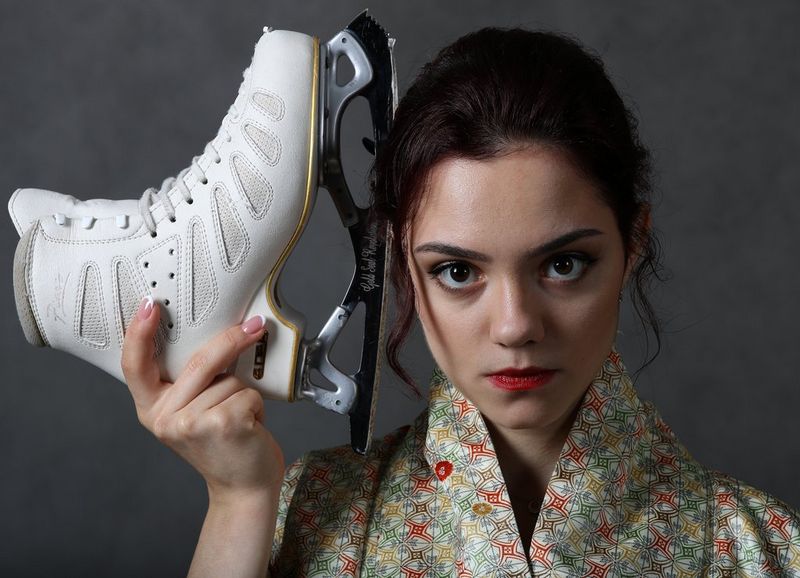La patineuse artistique russe Evgenia Medvedeva tient l'un de ses patins à côté de son visage tandis qu'elle regarde droit vers l'appareil photo.