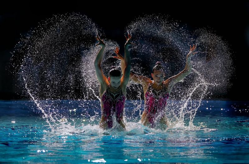 Deux femmes portant des maillots de bain rose et noir assortis nagent de façon synchronisée pendant une démonstration de natation.