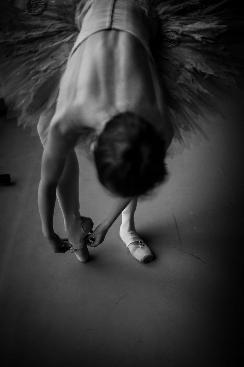 Un portrait en noir et blanc d'une ballerine se penchant pour enfiler ses collants sur sa chaussure de ballet.