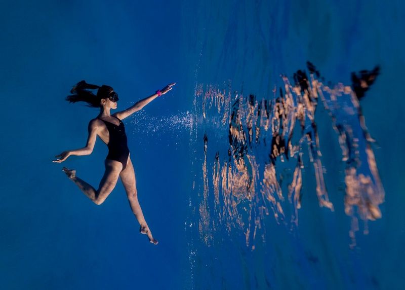 Une jeune instructrice de plongée sous-marine, portant une combinaison noire et un masque, pratique la plongée en apnée dans les eaux d'un bleu profond de la mer Rouge.