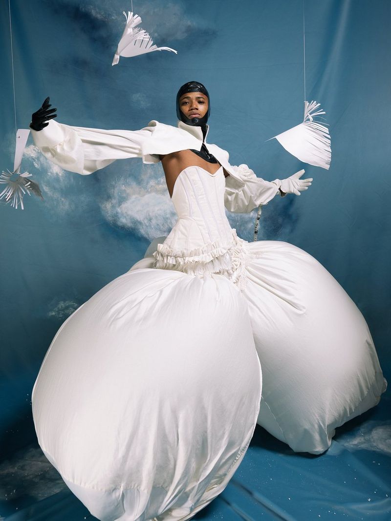 Une femme vêtue d'une robe blanche avec un pantalon bouffant pose sur un fond bleu.