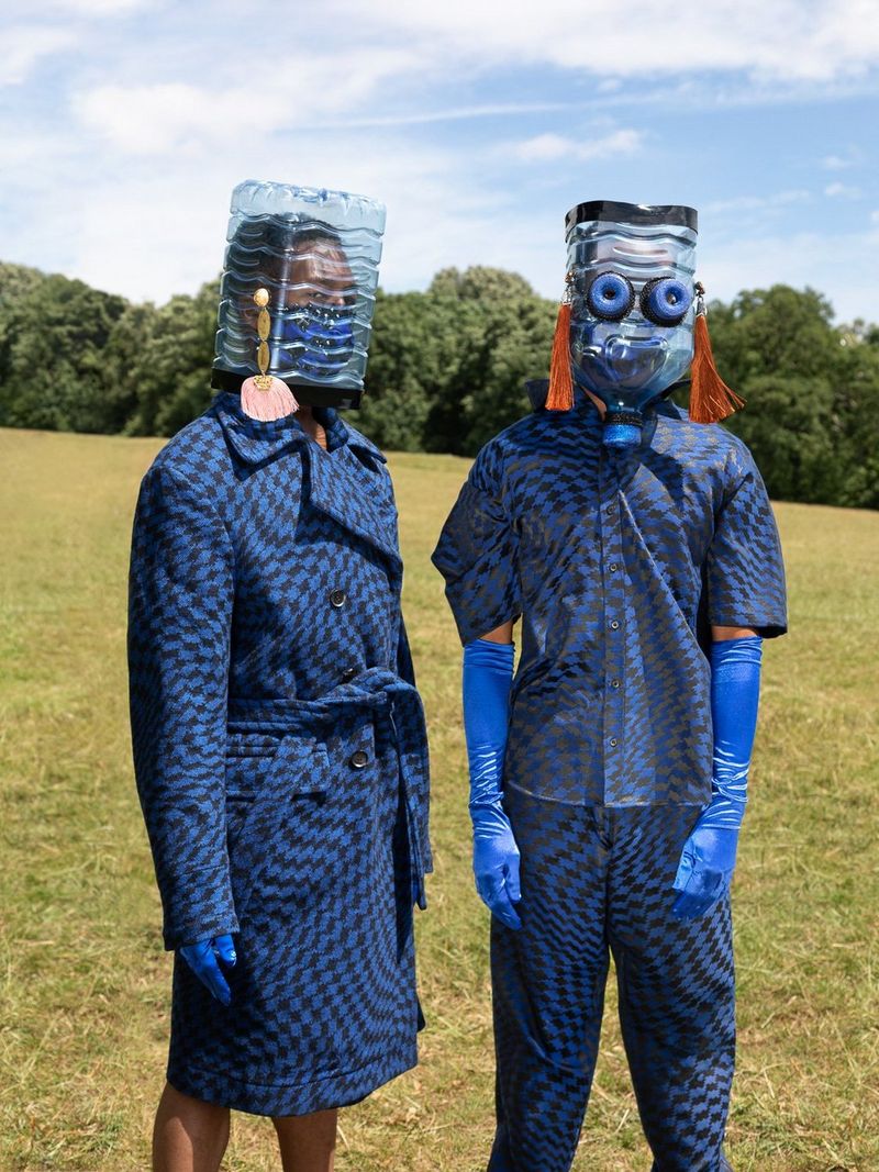 Deux modèles vêtus de bleu portant des gants en latex bleus et des masques en bouteilles d'eau en plastique.