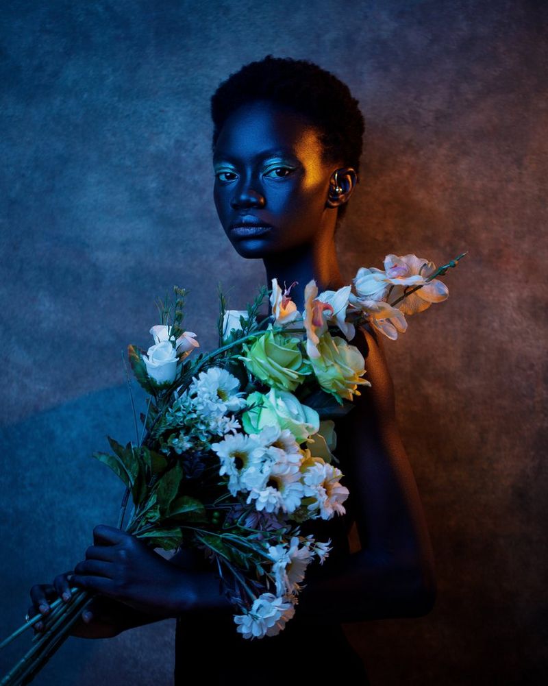 Photo de profil, au-dessus de la taille, d'une femme tournant la tête vers l'objectif. Elle porte un gros bouquet de fleurs blanches et roses, qui dissimule son torse.