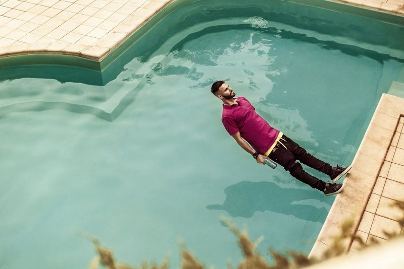 Un homme entièrement habillé semble suspendu dans les airs alors qu'il tombe en arrière dans une piscine.
